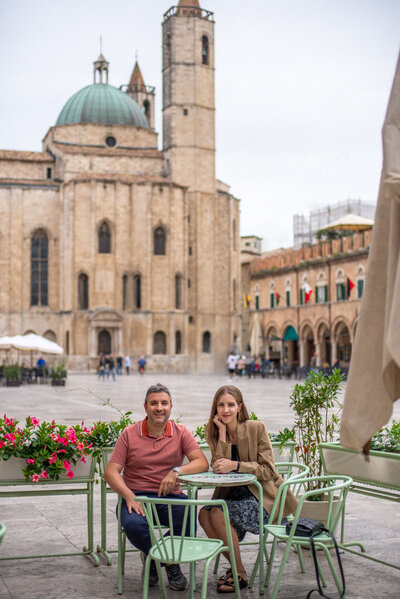Chantelle and Giovanni, couple and co-founders of The Italian on Tour sitting at a green table in an Italian plaza
