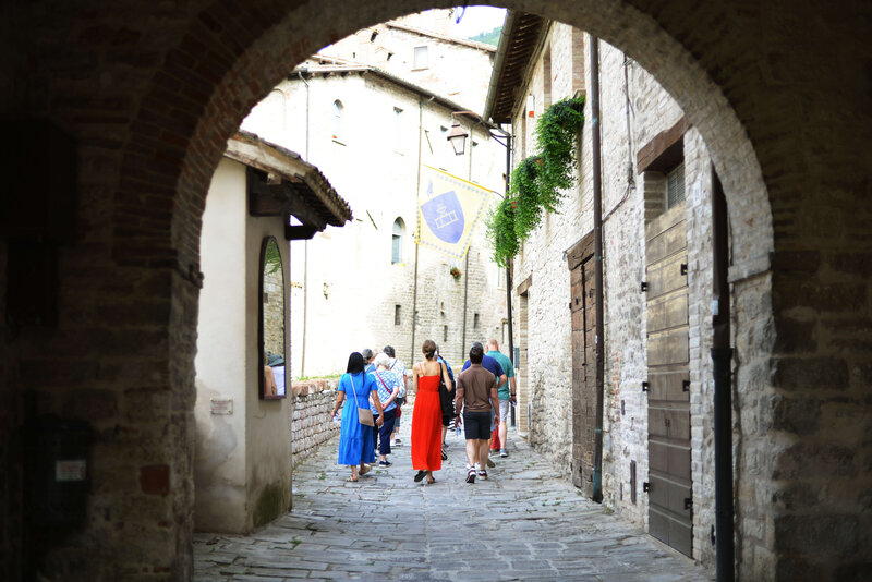 A group of travelers strolls through a charming, historic Italian village with stone streets and rustic buildings. This off-the-beaten-path Italy small group tour offers an authentic experience away from tourist crowds.