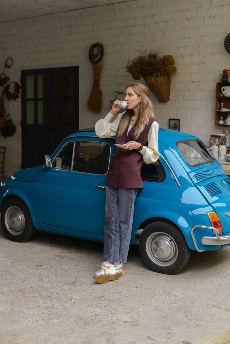 Chantelle, female co-founder of Italian on Tour enjoys an espresso beside a vintage blue car, a perfect moment from a relaxed Italy small group tour