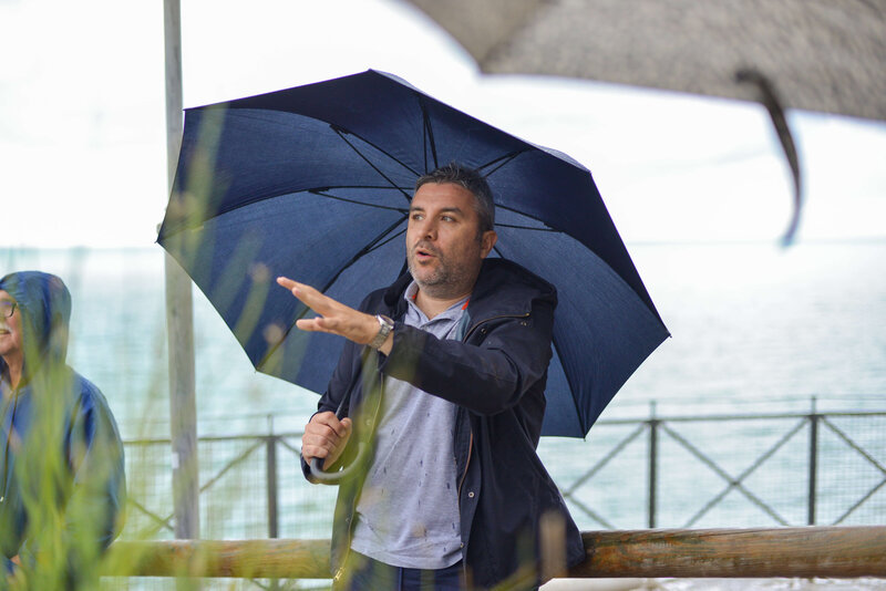 Giovanni, co-founder of The Italian on Tour, talking near the water and holding a blue umbrella