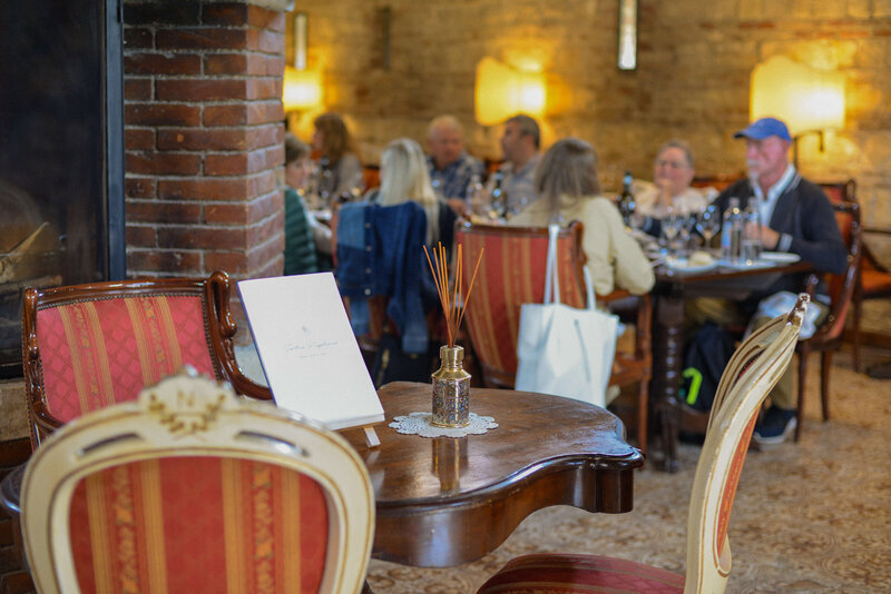 A cozy Italian restaurant with elegantly set tables, where a small group of travelers enjoys a meal. In the foreground, a wooden side table holds a reed diffuser and a menu, adding to the warm, inviting atmosphere of an intimate small group tour in Italy.