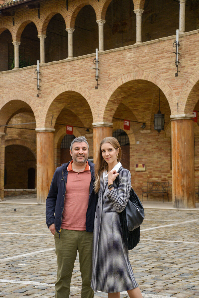 Giovanni and Chantelle, couple and co-founders stand in a stunning Italian courtyard with grand arches, capturing the warmth and hospitality of a small group Italy tour.
