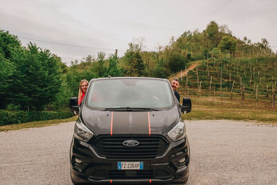 Two travelers stand beside a parked car, ready for a road trip in Italy, highlighting the need for an international driving permit.