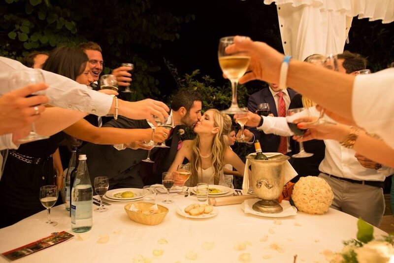 Travelers raise their glasses in a joyful toast during a food and wine tour in Italy, celebrating a shared meal under warm evening lights.